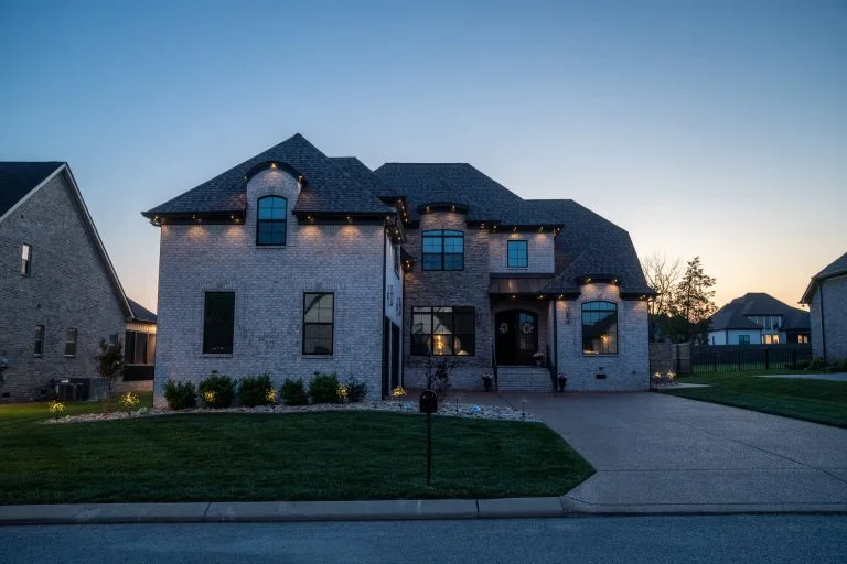 A beautifully lit brick house stands at dusk, surrounded by manicured lawns