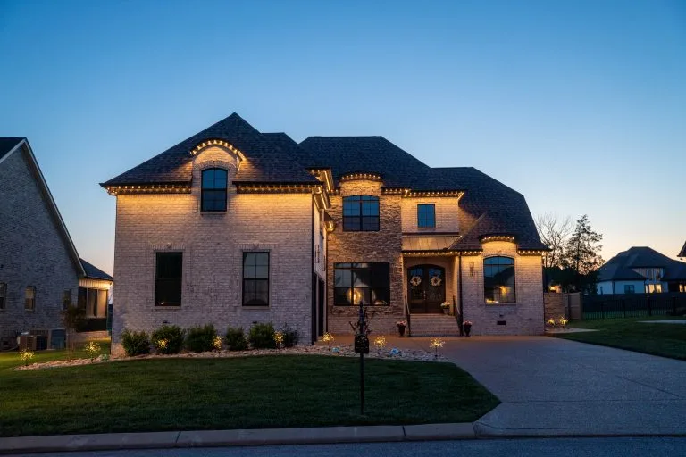 A beautifully lit brick house stands prominently against a twilight sky