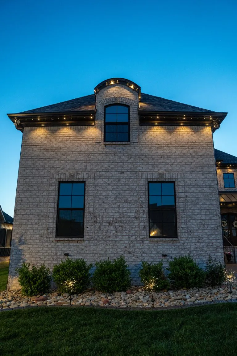 A brick house is illuminated with soft lights against a twilight sky