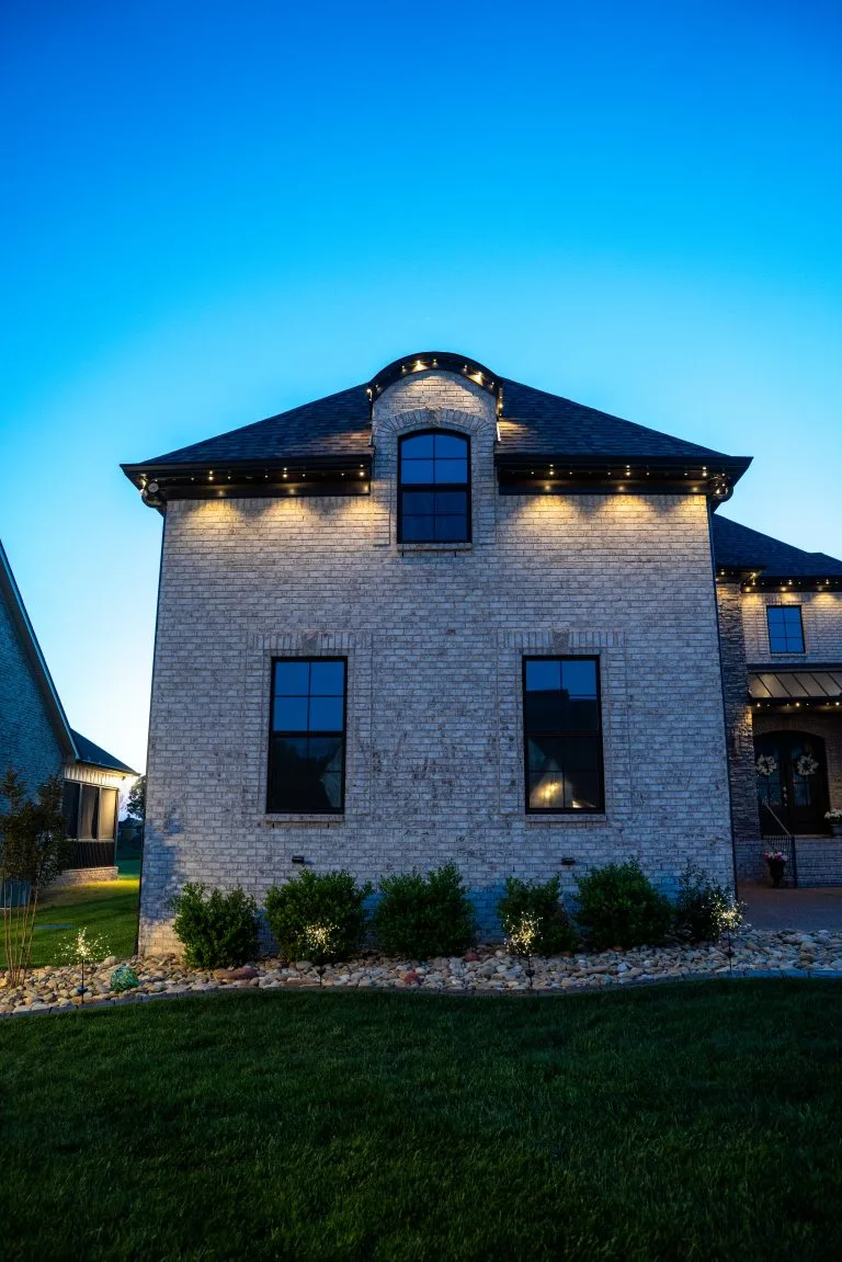 A brick house is illuminated by warm lights against a twilight sky