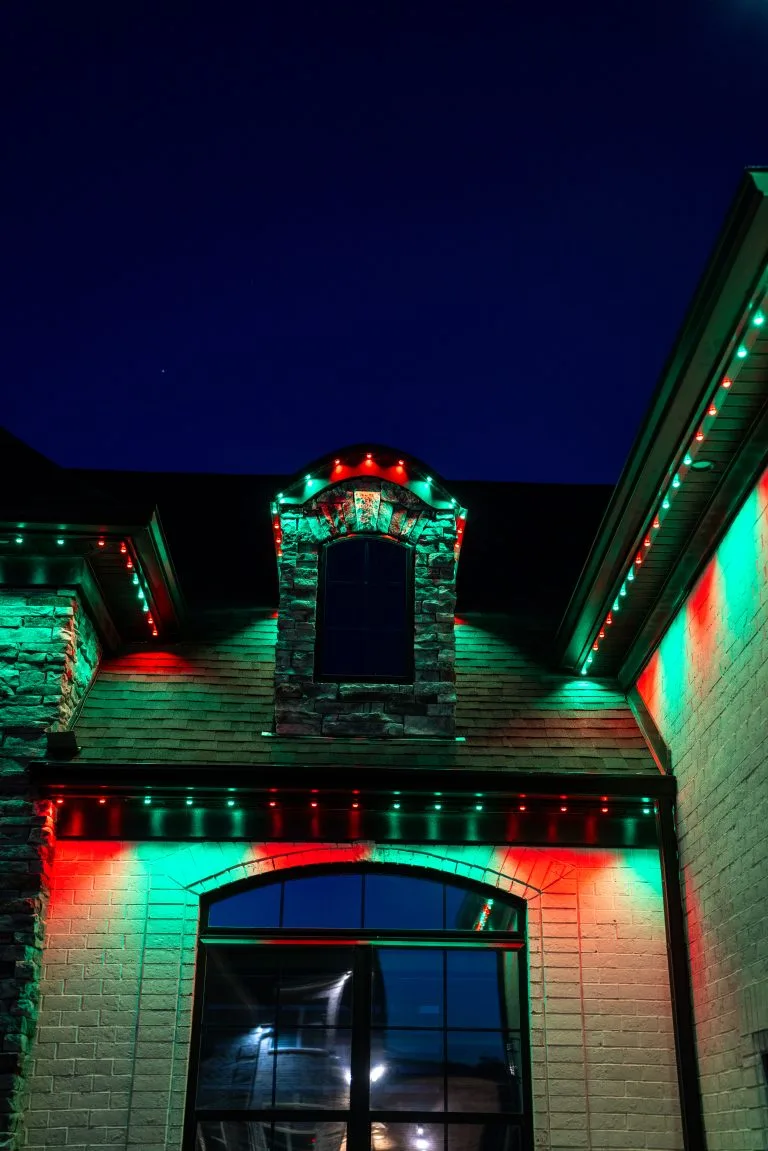 Bright red and green lights illuminate a house against a dark evening sky