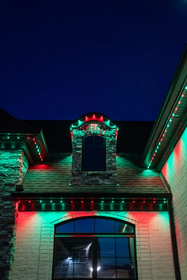 A house is adorned with vibrant red and green lights against a dark blue sky