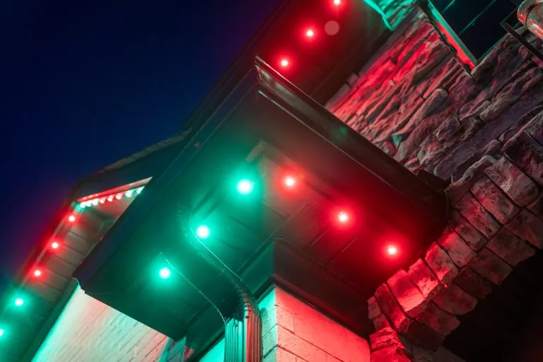 Vivid red and green lights illuminate the eaves of a stone house at dusk