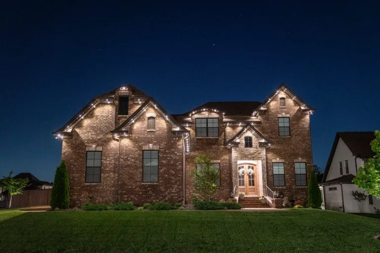 A beautifully lit brick house stands warmly against a darkening evening sky