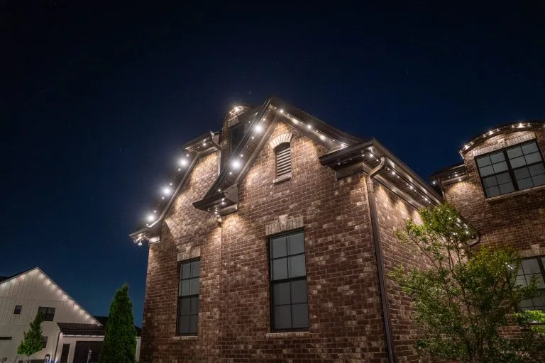 Warm holiday lights illuminate a brick house against a dark evening sky
