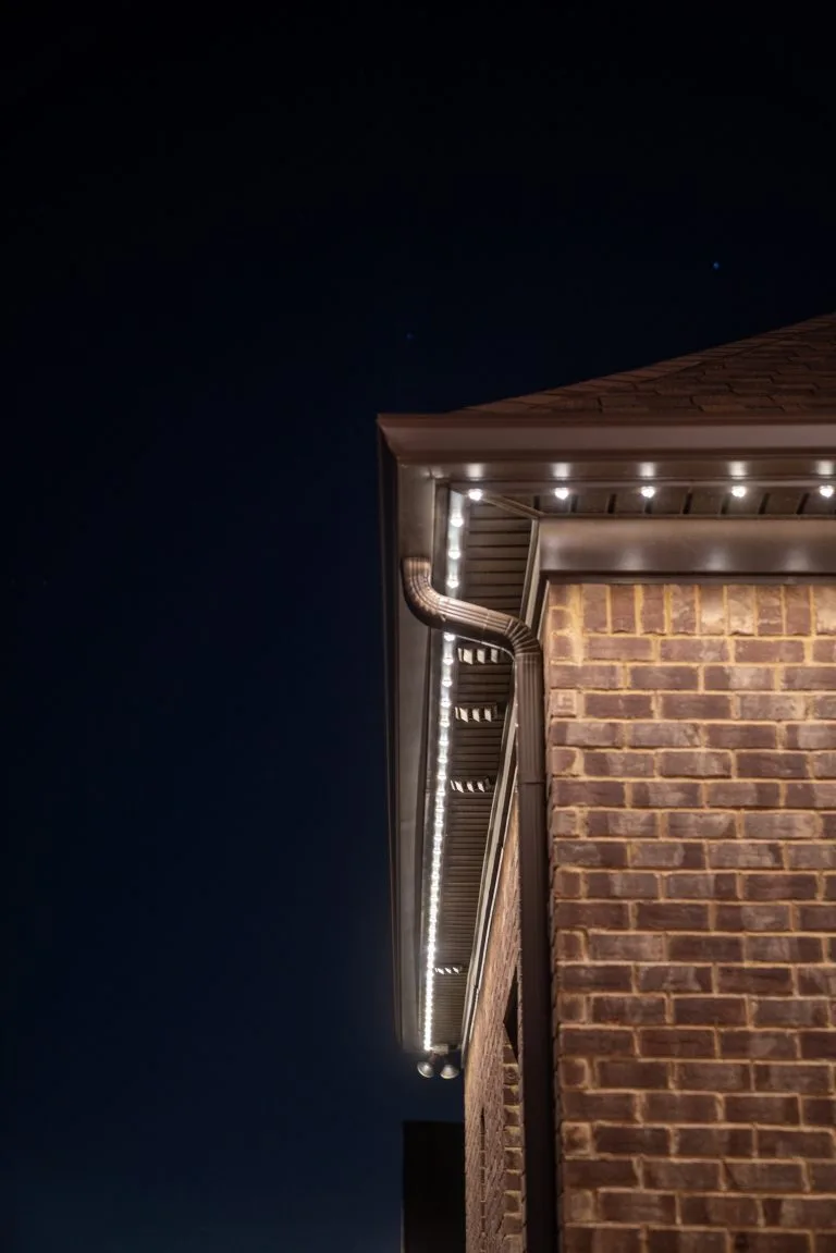 A brick house corner is adorned with soft, glowing LED lights against a dark night sky