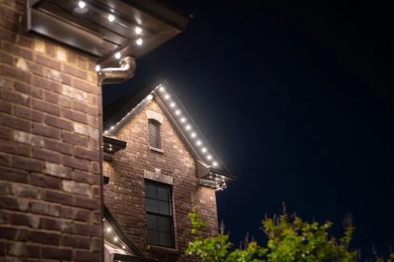 String lights illuminate a brick house against a dark night sky