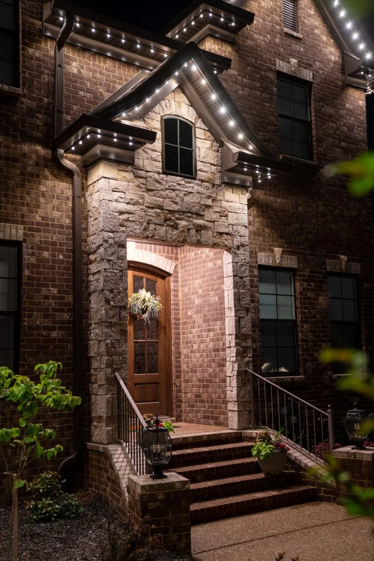 A warmly lit entrance features elegant stonework and bright holiday lights