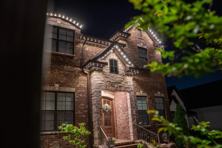 A beautifully lit brick house adorned with festive lighting in the evening