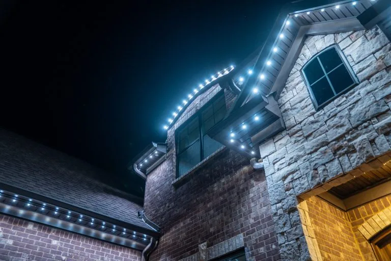 Bright white lights outline a house's architectural features against a dark night sky