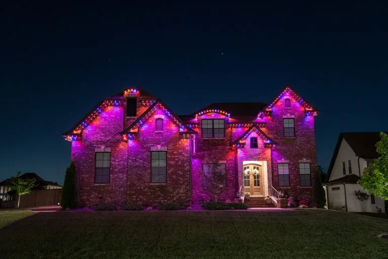 A large house is illuminated with vibrant purple lights against a dark night sky