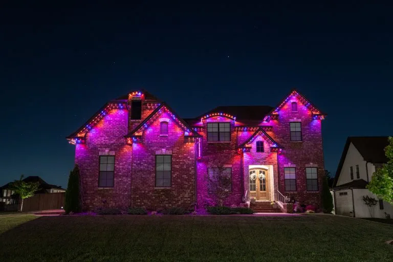 A house is illuminated with vibrant purple lights against a dark night sky