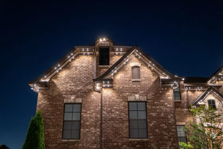 Twinkling lights adorn the brick facade of a house under a dark night sky