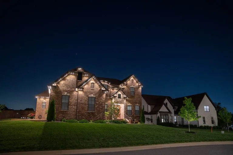 A beautifully lit brick house stands under a dark blue night sky