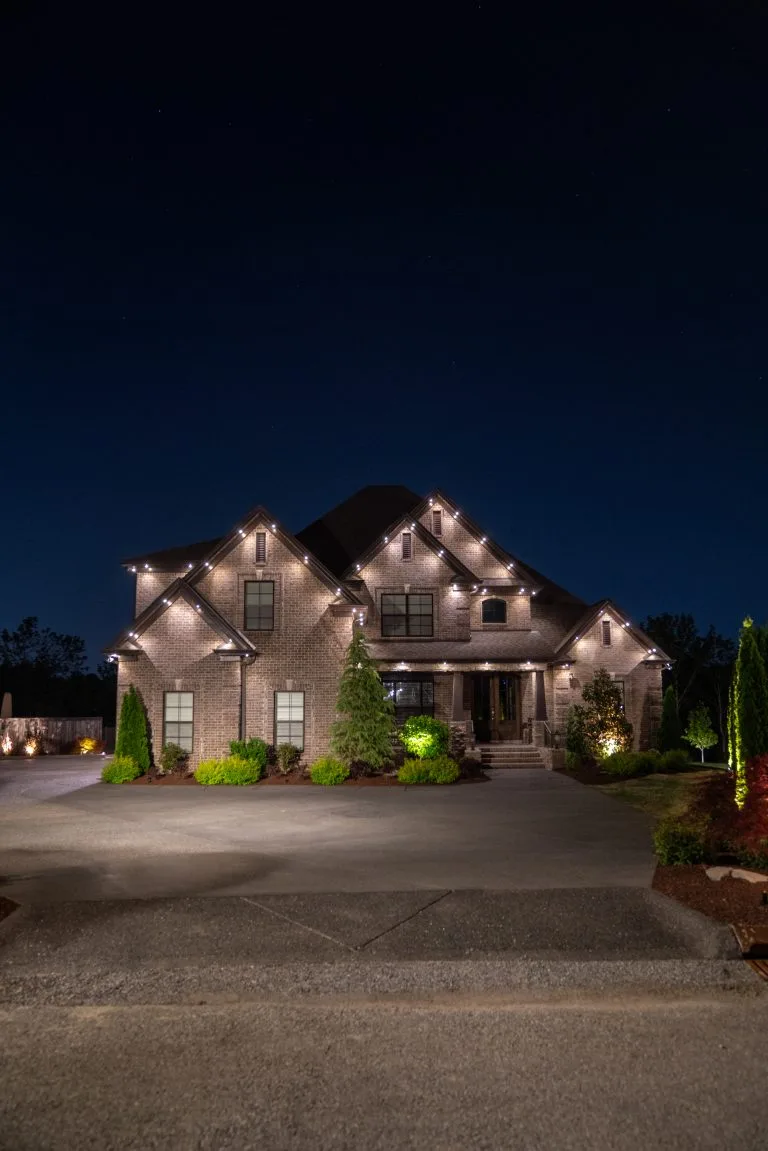 A beautifully lit house with elegant landscaping shines under the night sky