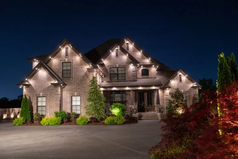 A beautifully lit, elegant home shines under the night sky, surrounded by greenery