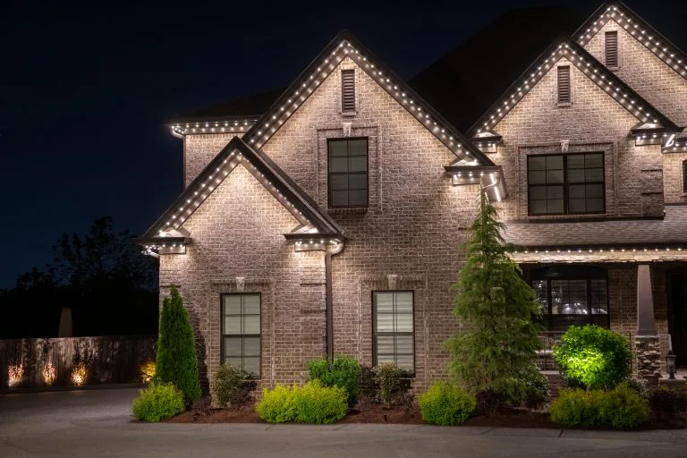 A well-lit brick house stands elegantly against a dark evening sky