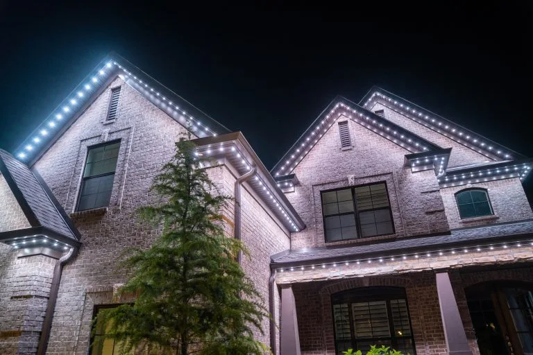 Bright decorative lights outline the rooftops of a well-lit brick house at night