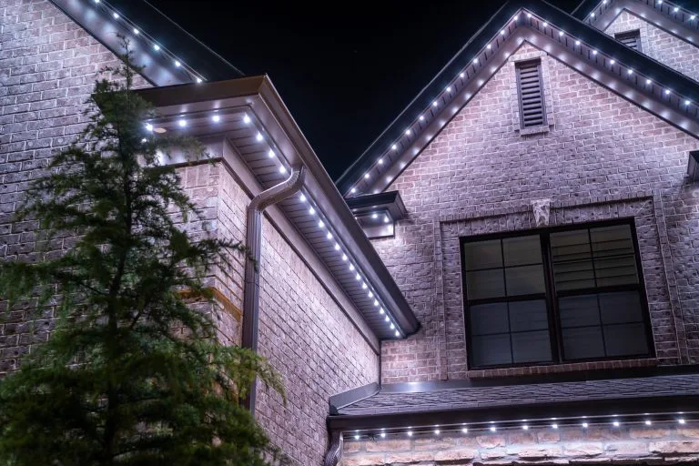 Twinkling white lights adorn the eaves of a brick house at night