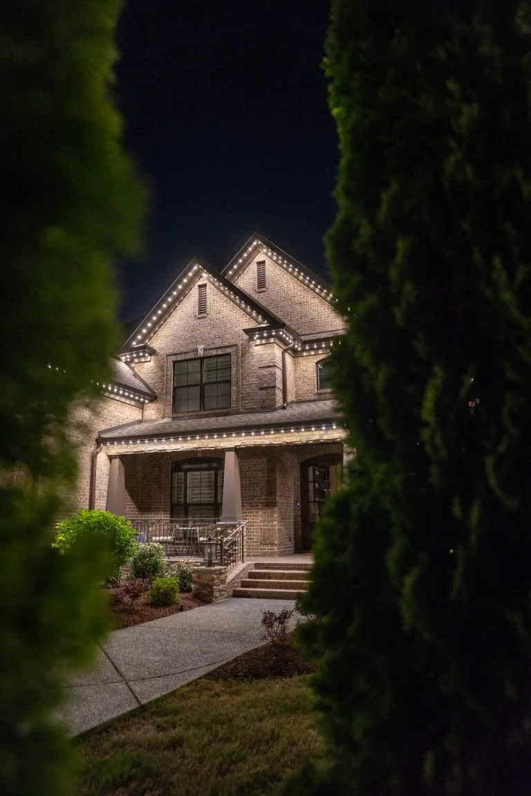 A beautifully illuminated house is framed by lush greenery at night