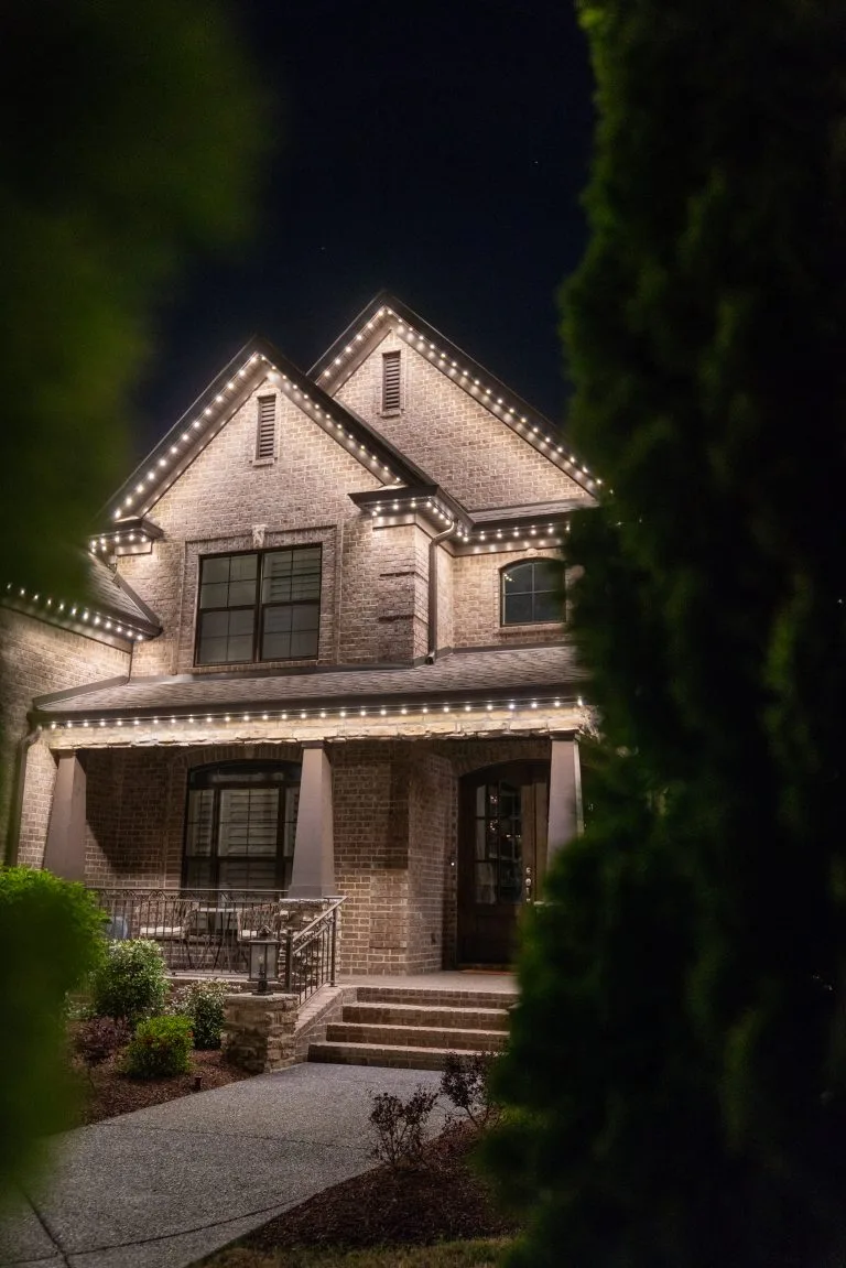 A beautifully lit house stands surrounded by greenery at night