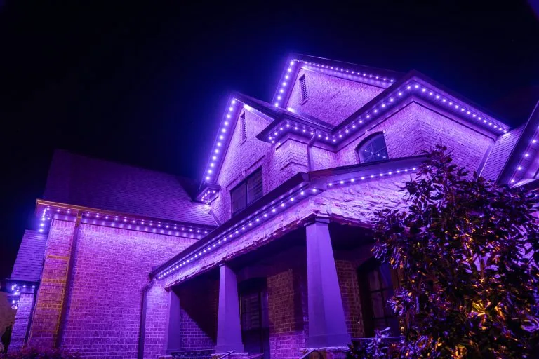 A house is vividly illuminated with purple lights against a dark night sky