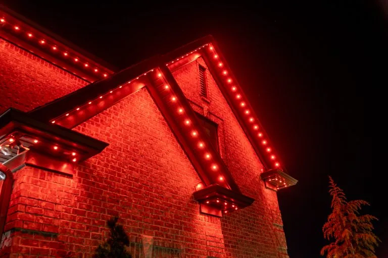 A house's roof glows with vibrant red lights against a dark night sky