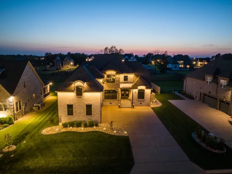 A beautifully lit house stands surrounded by landscaped gardens at twilight