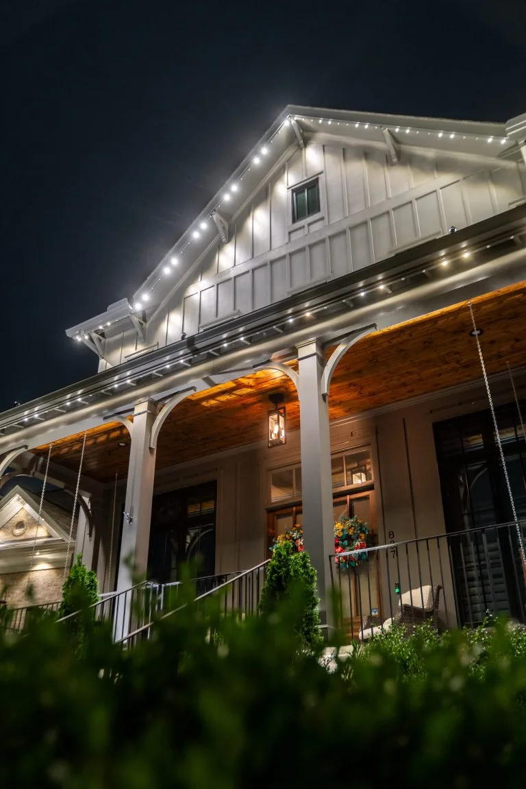A well-lit house features decorative lights along the roofline at night