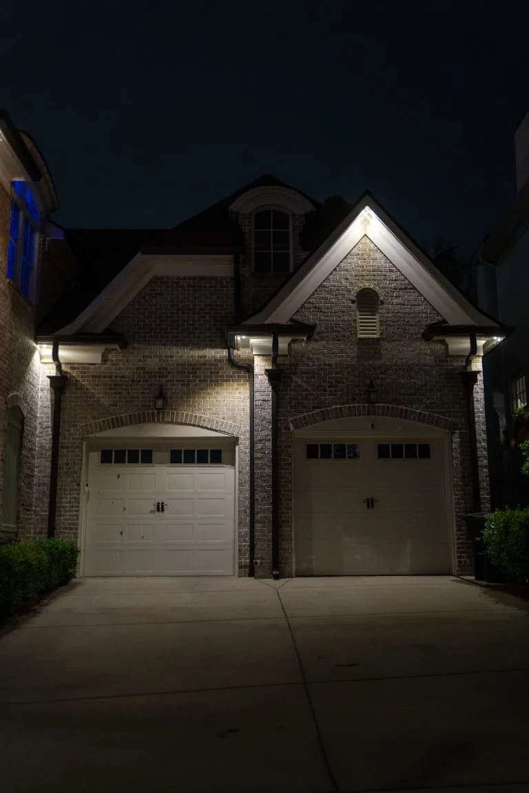 A dimly lit brick house with two garage doors under night sky illumination