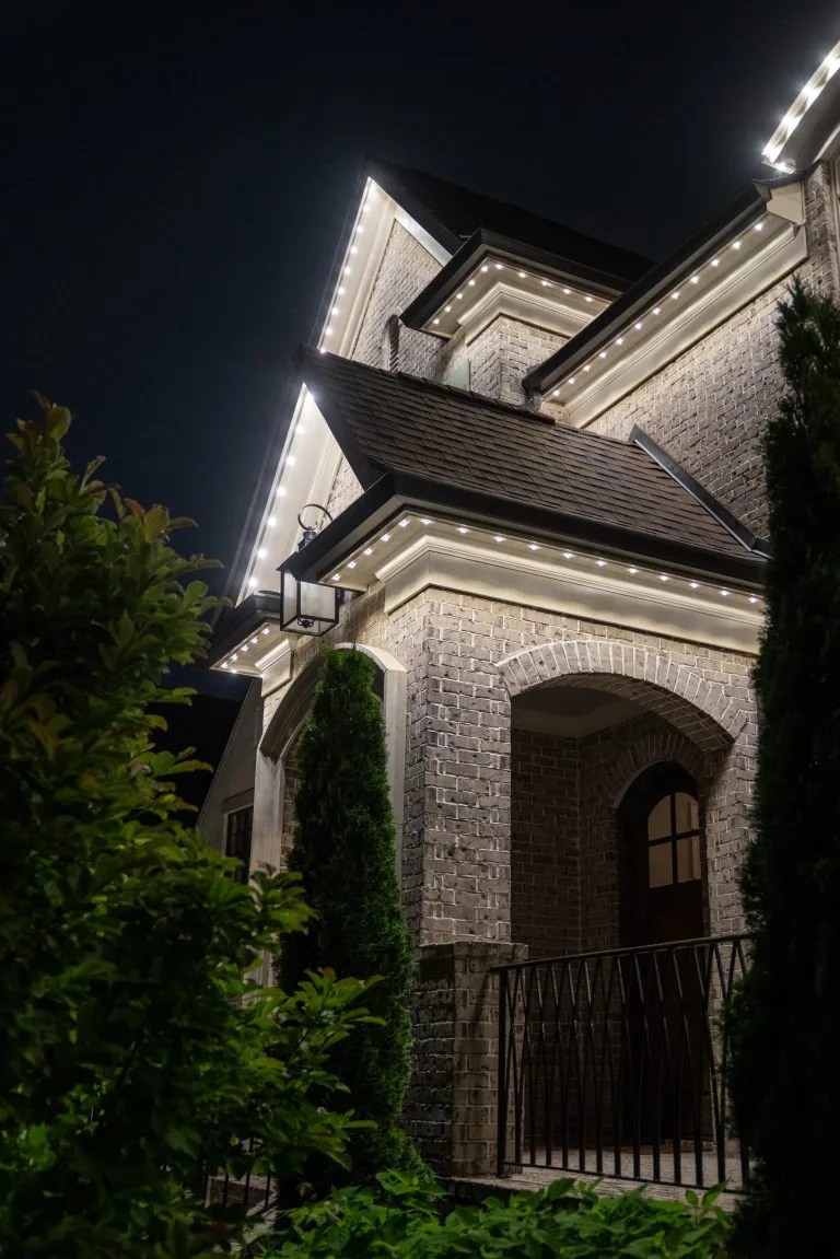A beautifully lit house at night showcases its architectural features and surrounding greenery