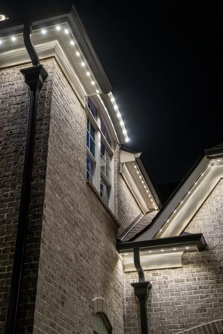 Warm white lights illuminate the architectural details of a brick home at night