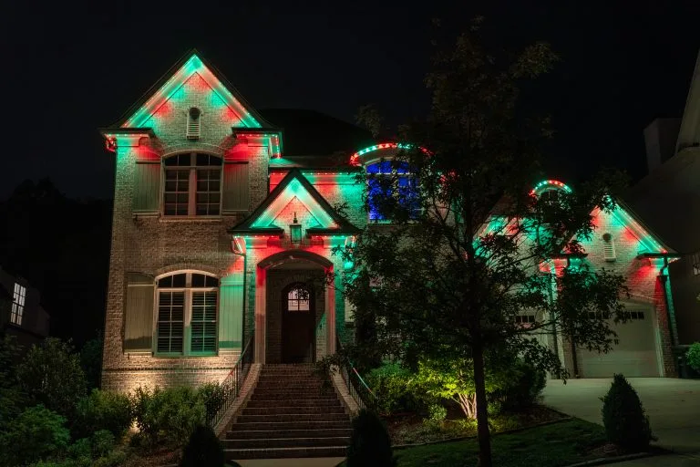 A beautifully decorated house is adorned with colorful red and green lights at night