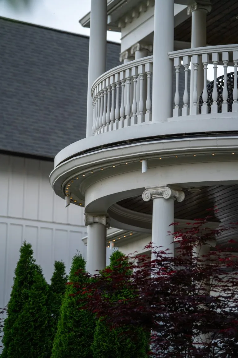 A gracefully curved balcony with white columns overlooks vibrant green shrubs