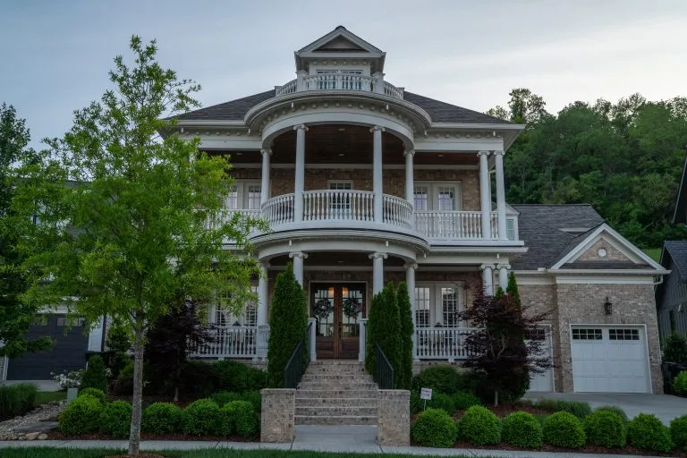 A grand house features a circular porch, lush greenery, and elegant architectural details