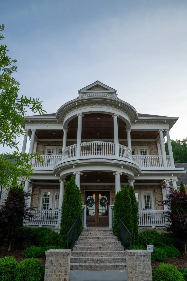 A grand, multi-tiered house features elegant balconies and lush greenery