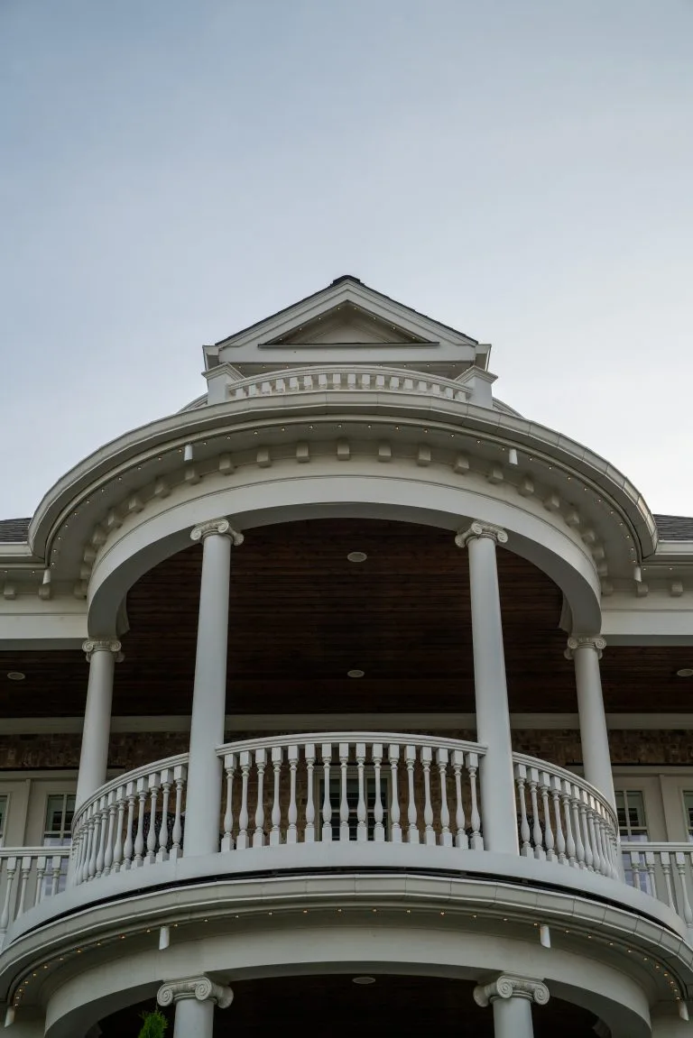 A grand, white-columned porch curves prominently under a clear blue sky