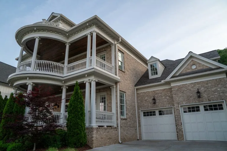 A large, elegant house features a curved balcony and two garage doors