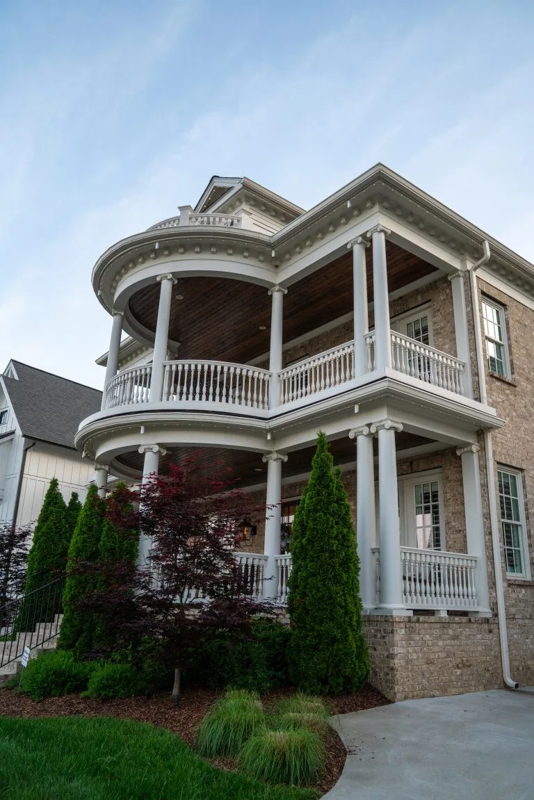 A beautifully constructed brick house features a grand curved porch and lush greenery