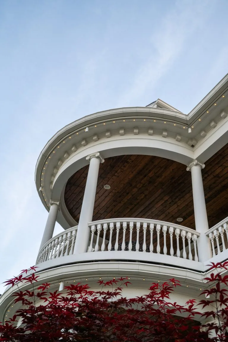 A curved balcony with white railings overlooks vibrant red foliage against a blue sky