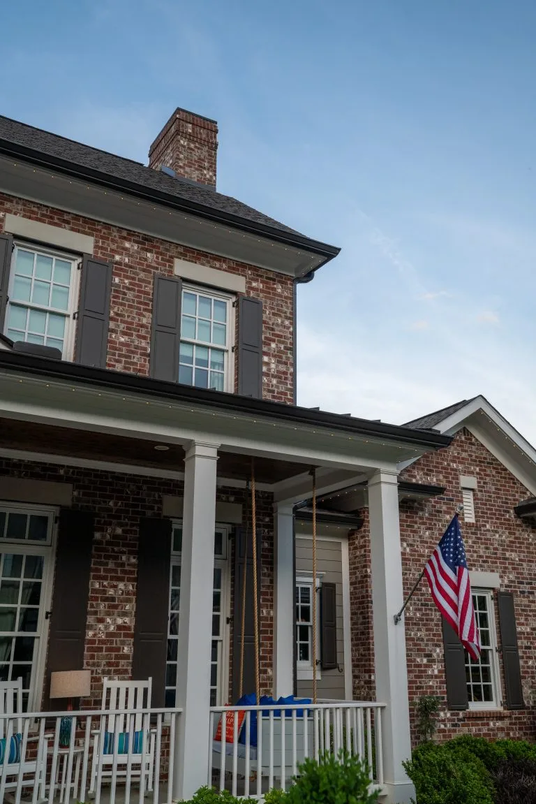 A two-story brick house features a front porch and a waving American flag