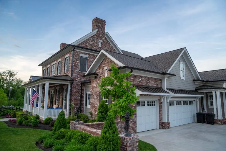 A well-kept suburban home features brick accents, a manicured lawn, and American flags