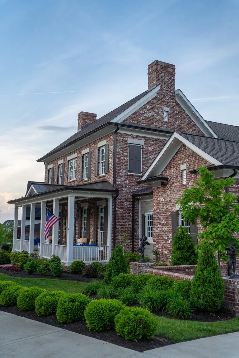 A charming brick house features a front porch and manicured landscaping under a clear sky