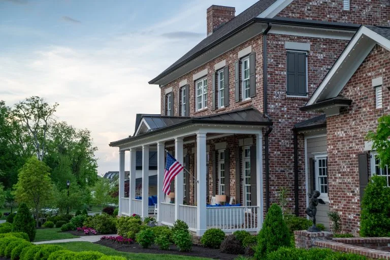A charming brick house features a porch with an American flag and well-kept landscaping