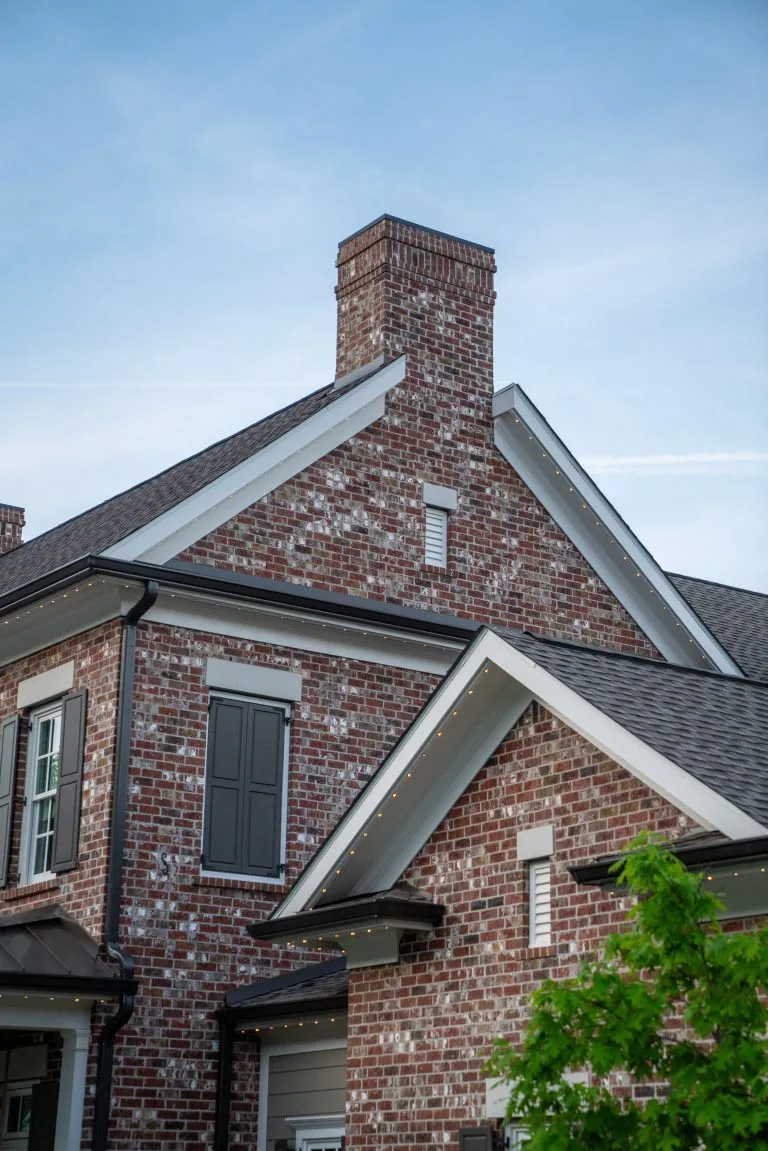 A brick house features a prominent chimney and contrast between dark and light elements