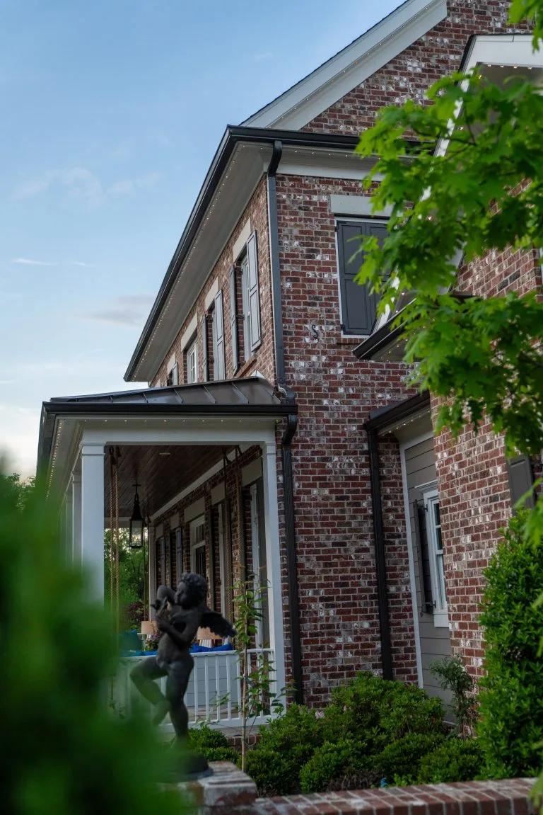 A brick house features a statue and a person sitting on the porch