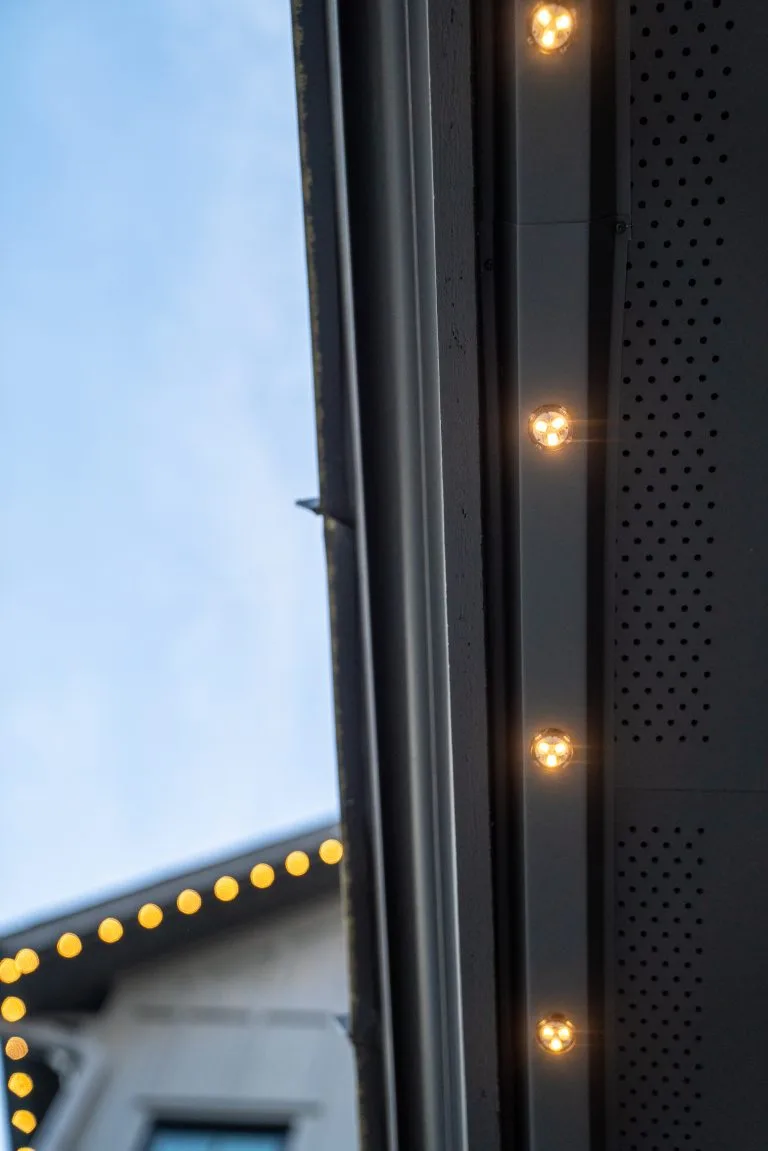 Softly glowing string lights illuminate a building against a clear blue sky