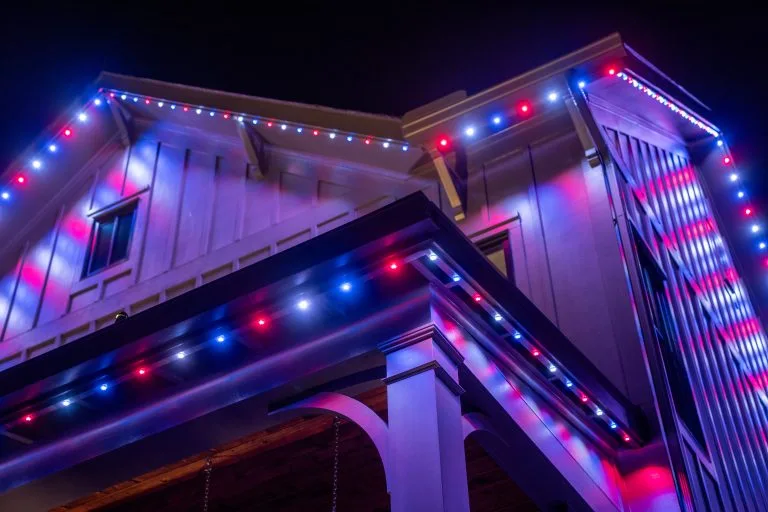 Colorful lights illuminate the exterior of a house against a dark night sky