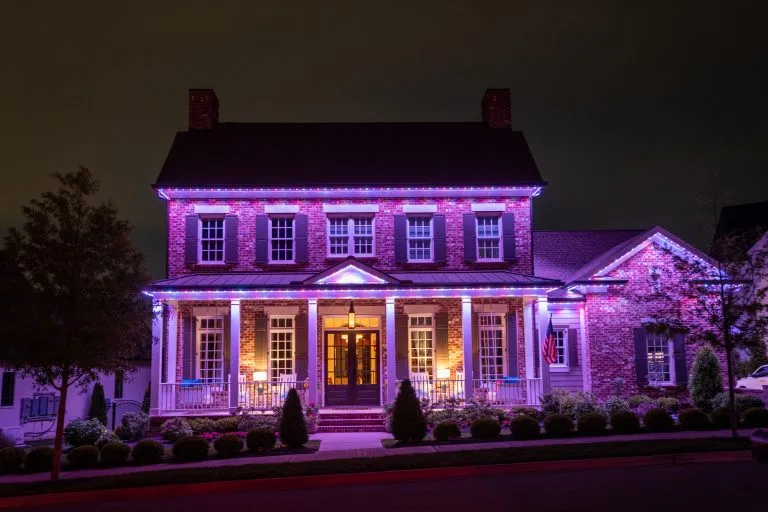 A beautifully illuminated brick house displays vibrant purple lights against a dark sky