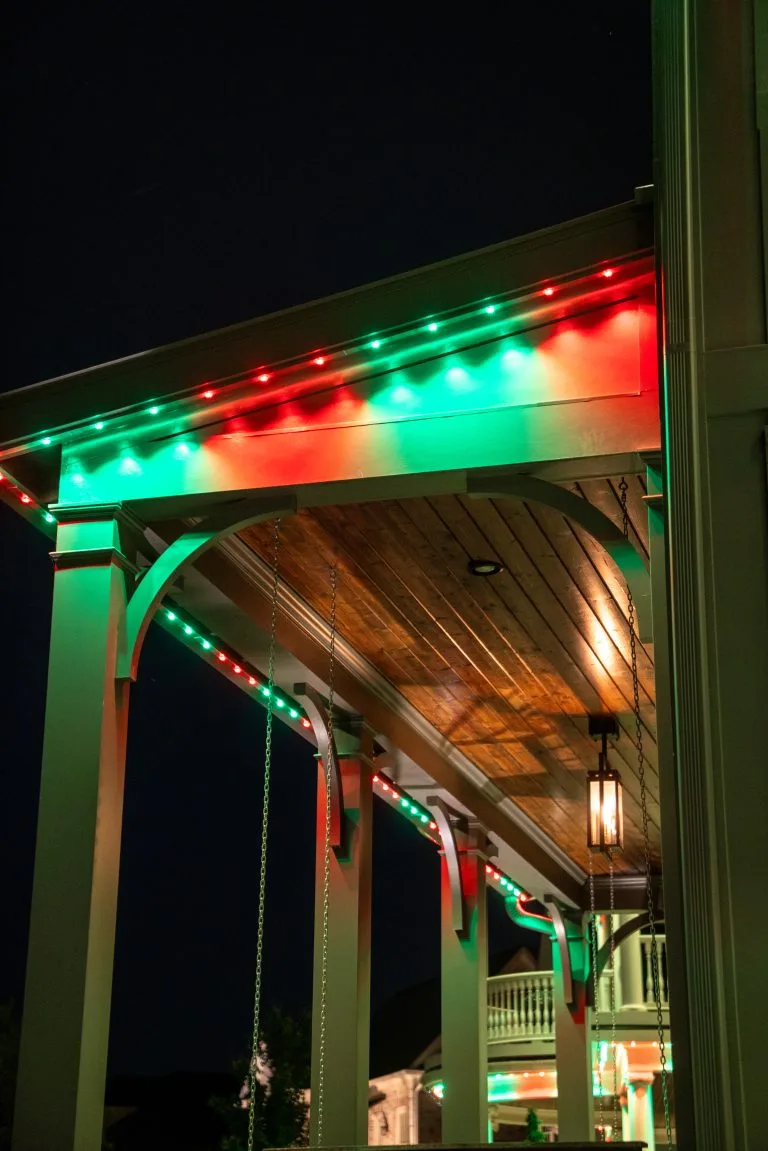 A porch is decorated with green and red lights, creating a festive atmosphere